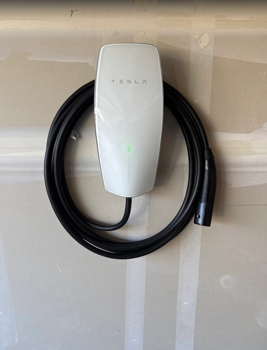 Tesla Wall Connector mounted on a garage wall with the charging cable neatly coiled