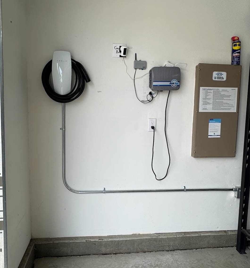 Tesla home charger with surface conduit routed along the garage wall beside an electrical panel