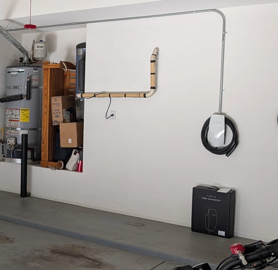 Tesla Wall Connector in a garage with conduit running overhead and down to the charger